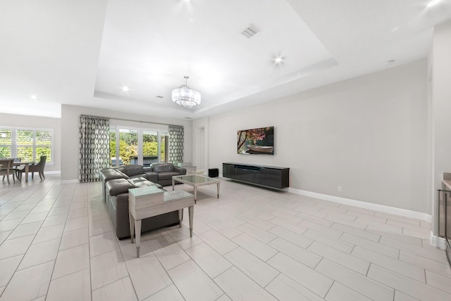 tiled living room featuring a chandelier and a raised ceiling