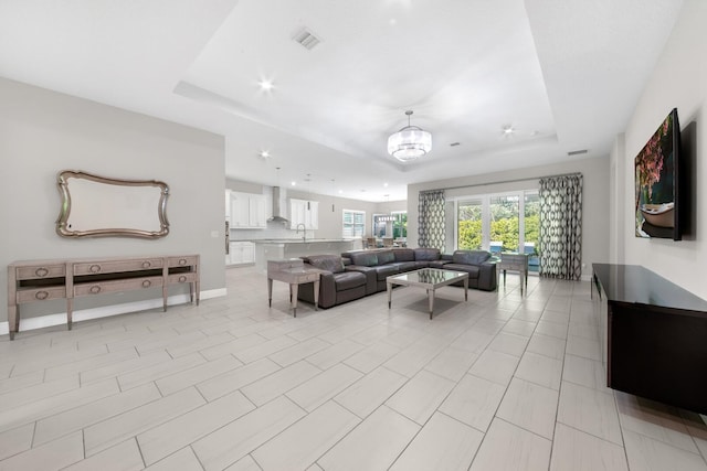 living room featuring light tile patterned floors, an inviting chandelier, a raised ceiling, and sink