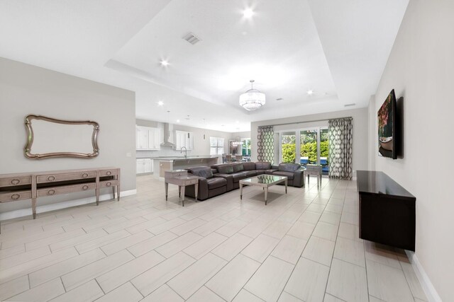 tiled living room featuring a notable chandelier, a raised ceiling, and sink