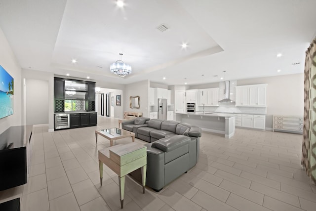 tiled living room featuring an inviting chandelier, a tray ceiling, wine cooler, and sink