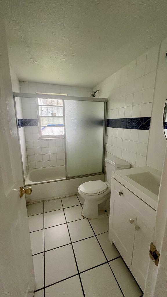 full bathroom featuring vanity, shower / bath combination with glass door, tile patterned flooring, toilet, and tile walls