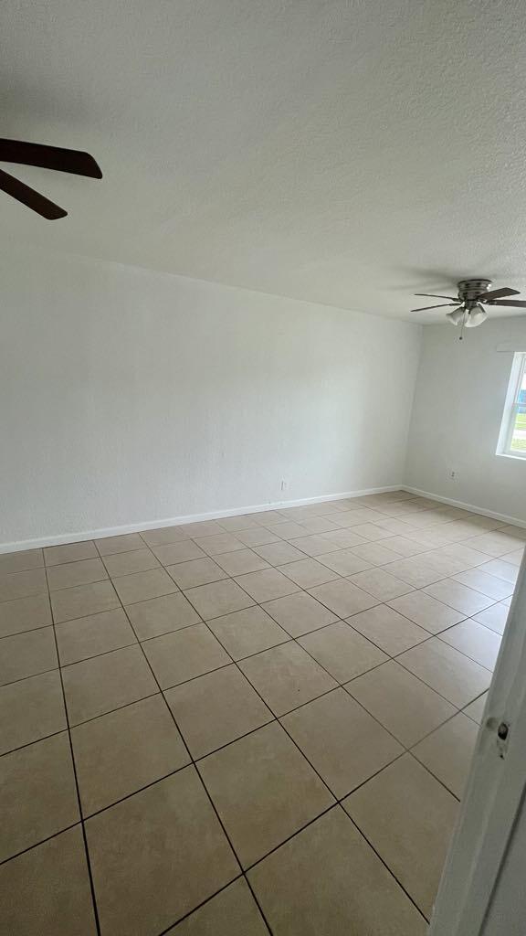 tiled empty room featuring ceiling fan and a textured ceiling