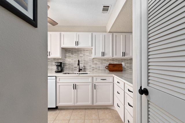 kitchen featuring tasteful backsplash, light tile patterned floors, sink, white dishwasher, and white cabinetry