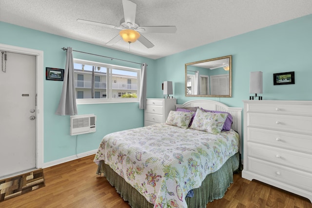 bedroom with hardwood / wood-style floors, ceiling fan, an AC wall unit, and a textured ceiling