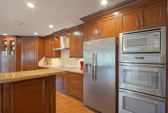 kitchen with light stone counters, light hardwood / wood-style flooring, stainless steel appliances, and wall chimney range hood