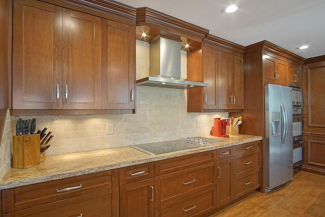 kitchen featuring wall chimney exhaust hood, decorative backsplash, light stone countertops, light wood-type flooring, and stainless steel appliances