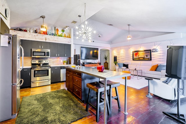 kitchen featuring a breakfast bar area, open floor plan, vaulted ceiling, appliances with stainless steel finishes, and decorative backsplash