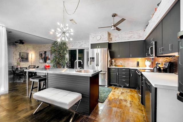 kitchen featuring brick wall, stainless steel appliances, light countertops, a sink, and ceiling fan with notable chandelier