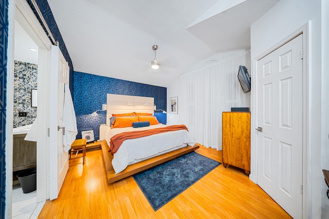 bedroom with lofted ceiling, wood finished floors, and wallpapered walls