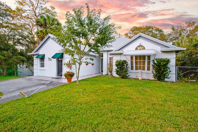 view of front of house with a front yard, concrete driveway, fence, and stucco siding