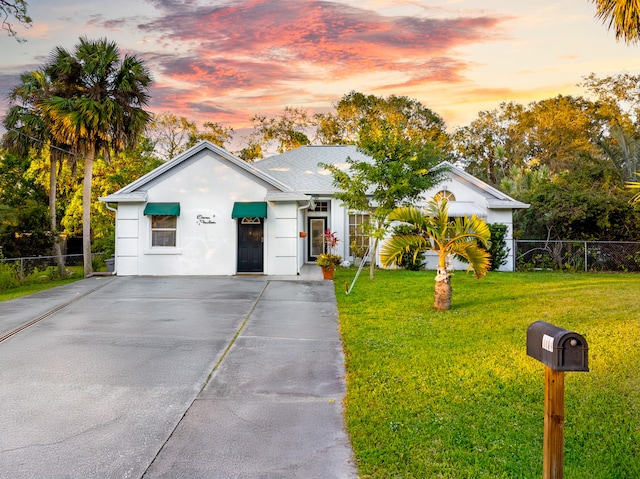 ranch-style home featuring a yard, fence, driveway, and stucco siding