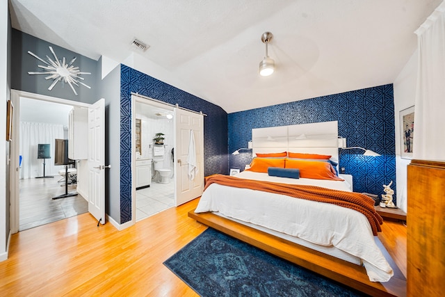 bedroom featuring vaulted ceiling, an accent wall, wood finished floors, and wallpapered walls