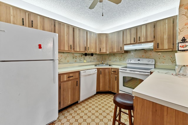 kitchen with white appliances, sink, ceiling fan, a textured ceiling, and a breakfast bar area