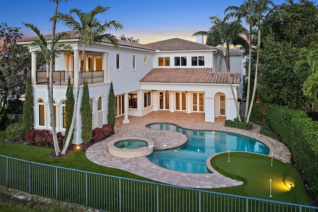 back house at dusk with a pool with hot tub, a balcony, a patio, and french doors