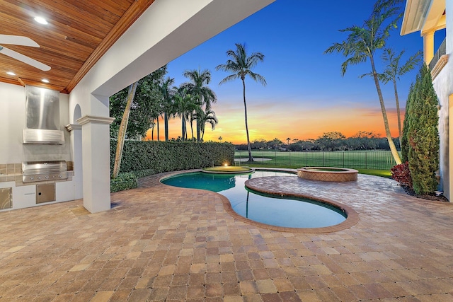 pool at dusk with an in ground hot tub, a patio, an outdoor kitchen, and grilling area