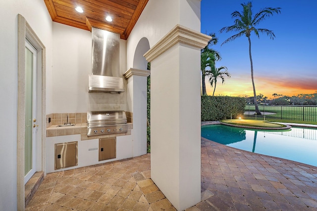 pool at dusk with an outdoor kitchen, area for grilling, and sink