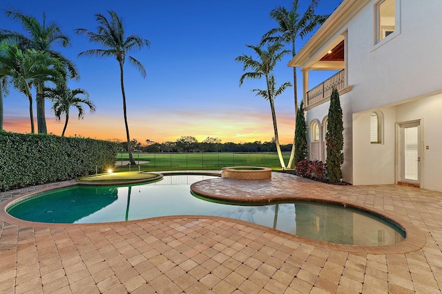 pool at dusk featuring a patio area and an in ground hot tub