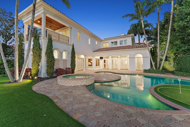 rear view of property featuring a swimming pool with hot tub, a balcony, and a patio area