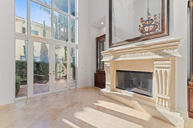 unfurnished living room featuring a premium fireplace, a towering ceiling, a chandelier, and french doors