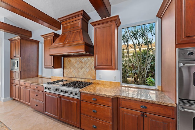 kitchen with beamed ceiling, appliances with stainless steel finishes, light stone countertops, and custom range hood