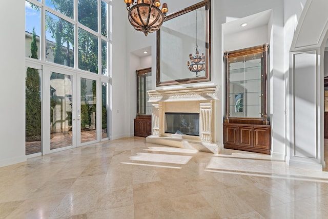 unfurnished living room with a notable chandelier, a premium fireplace, a high ceiling, and french doors