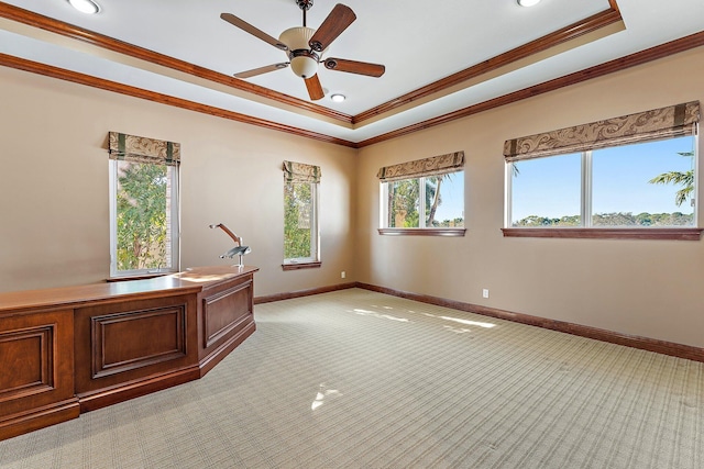 unfurnished office featuring ceiling fan, light colored carpet, ornamental molding, and a tray ceiling