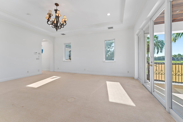 empty room featuring a chandelier, a tray ceiling, a healthy amount of sunlight, and light colored carpet