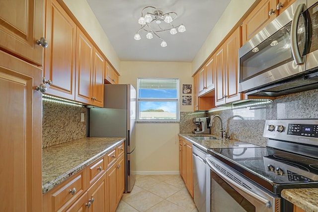 kitchen with light tile patterned flooring, light stone countertops, a sink, appliances with stainless steel finishes, and decorative backsplash