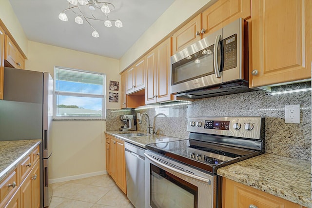 kitchen featuring light stone counters, light tile patterned flooring, a sink, appliances with stainless steel finishes, and decorative backsplash