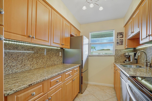 kitchen with light stone counters, a sink, appliances with stainless steel finishes, and baseboards