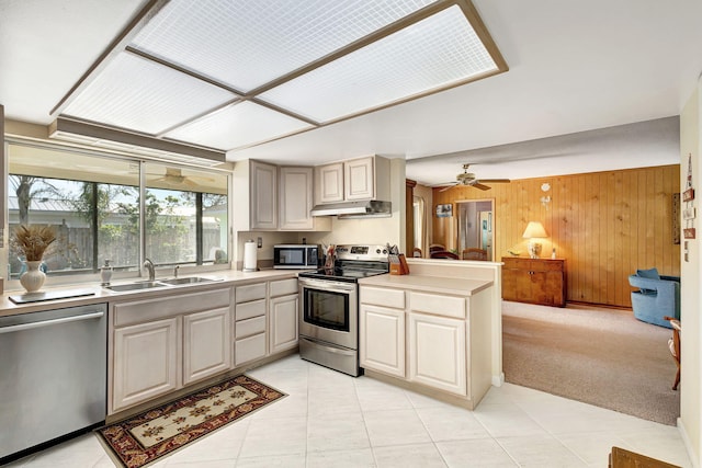 kitchen featuring light carpet, appliances with stainless steel finishes, ceiling fan, sink, and wood walls