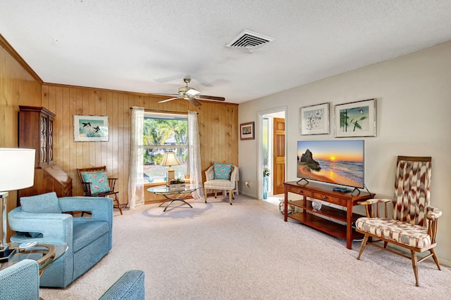 living area with a textured ceiling, light colored carpet, ceiling fan, and wooden walls