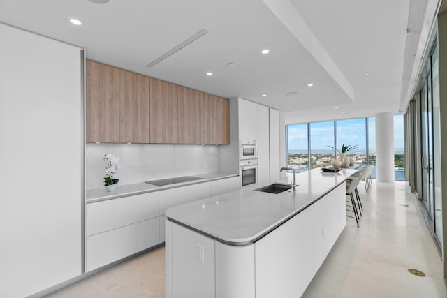 kitchen featuring sink, a center island with sink, white cabinetry, and a wall of windows