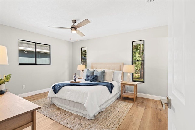 bedroom with a textured ceiling, ceiling fan, multiple windows, and light hardwood / wood-style flooring