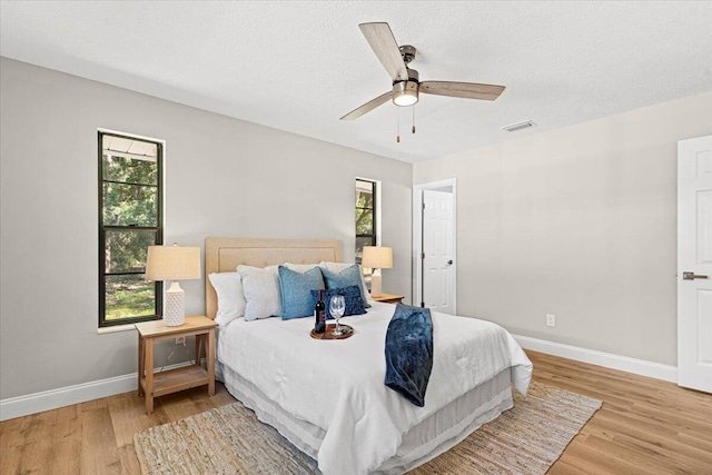 bedroom featuring a textured ceiling, ceiling fan, multiple windows, and light hardwood / wood-style flooring