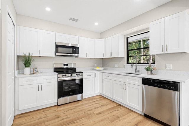 kitchen featuring sink, light wood-type flooring, appliances with stainless steel finishes, light stone counters, and white cabinetry