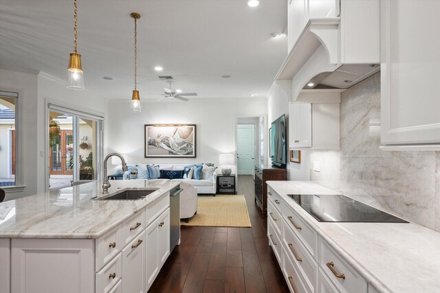 kitchen featuring white cabinets, decorative light fixtures, sink, backsplash, and a center island with sink