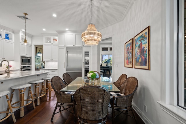 dining space featuring dark wood-type flooring, crown molding, an inviting chandelier, and sink