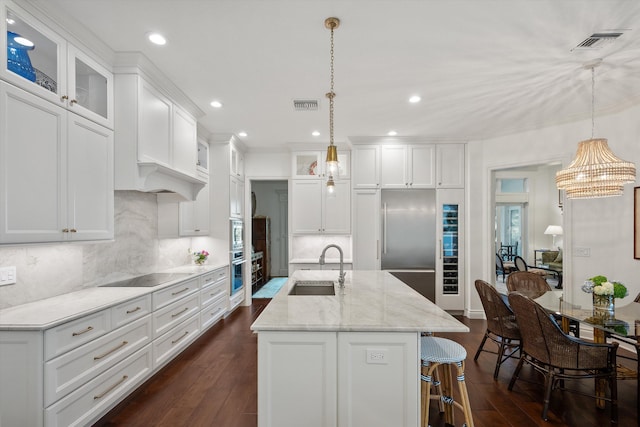 kitchen with hanging light fixtures, white cabinets, sink, and built in appliances