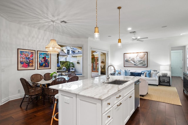 kitchen with a center island with sink, ceiling fan with notable chandelier, white cabinets, light stone counters, and sink