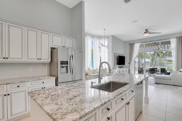 kitchen with sink, appliances with stainless steel finishes, light stone countertops, ceiling fan with notable chandelier, and backsplash