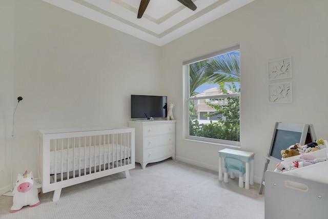 bedroom featuring a nursery area, light carpet, and ceiling fan