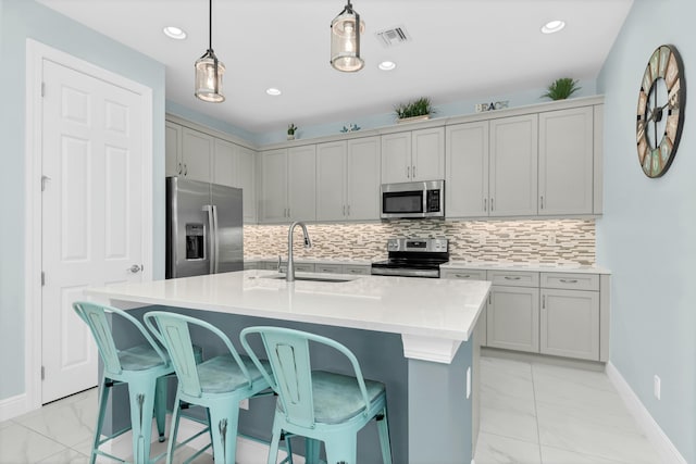 kitchen with sink, appliances with stainless steel finishes, hanging light fixtures, tasteful backsplash, and a center island with sink