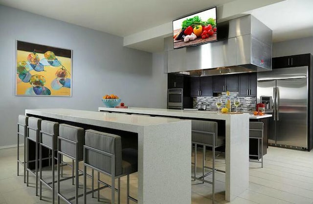 kitchen featuring extractor fan, tasteful backsplash, a center island, appliances with stainless steel finishes, and a kitchen breakfast bar