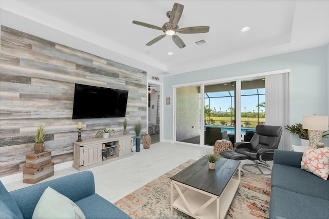 living room featuring a tray ceiling, ceiling fan, and wood walls