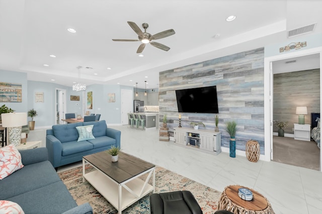 living room featuring ceiling fan with notable chandelier and a raised ceiling