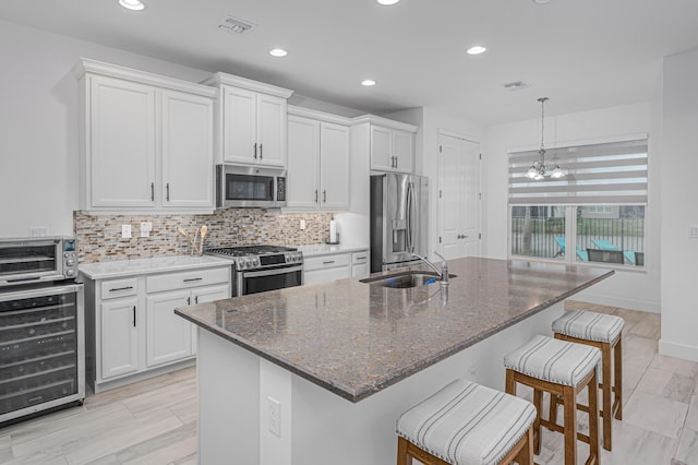 kitchen featuring wine cooler, stainless steel appliances, a center island with sink, and white cabinets