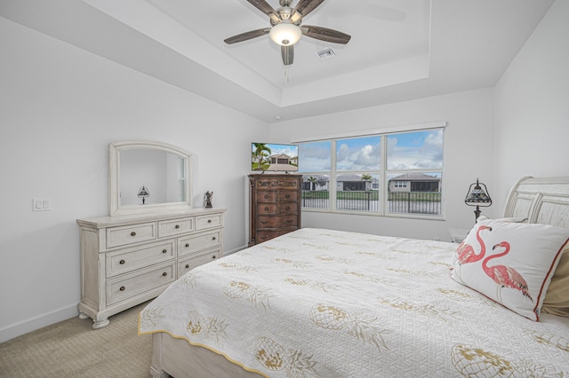 bedroom with light carpet, ceiling fan, and a tray ceiling