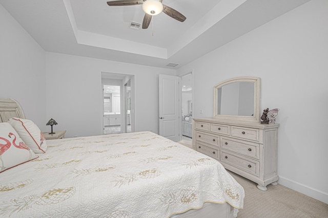 carpeted bedroom with ensuite bath, a raised ceiling, and ceiling fan