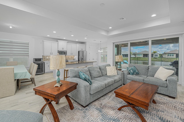 living room with wine cooler, a tray ceiling, and light wood-type flooring